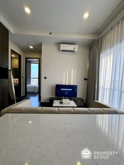 Modern living room with sleek design and natural light, featuring a cozy seating area and wall-mounted TV.