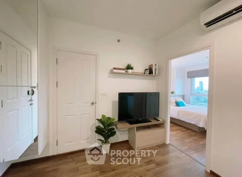 Modern apartment interior with TV and bedroom view, featuring wooden flooring and air conditioning.