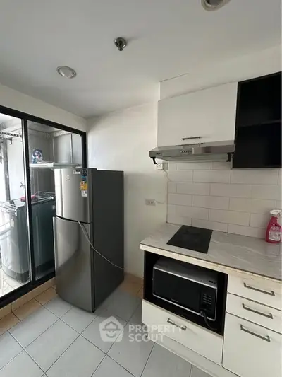Modern kitchen with sleek appliances and open layout, featuring a fridge, microwave, and stovetop.