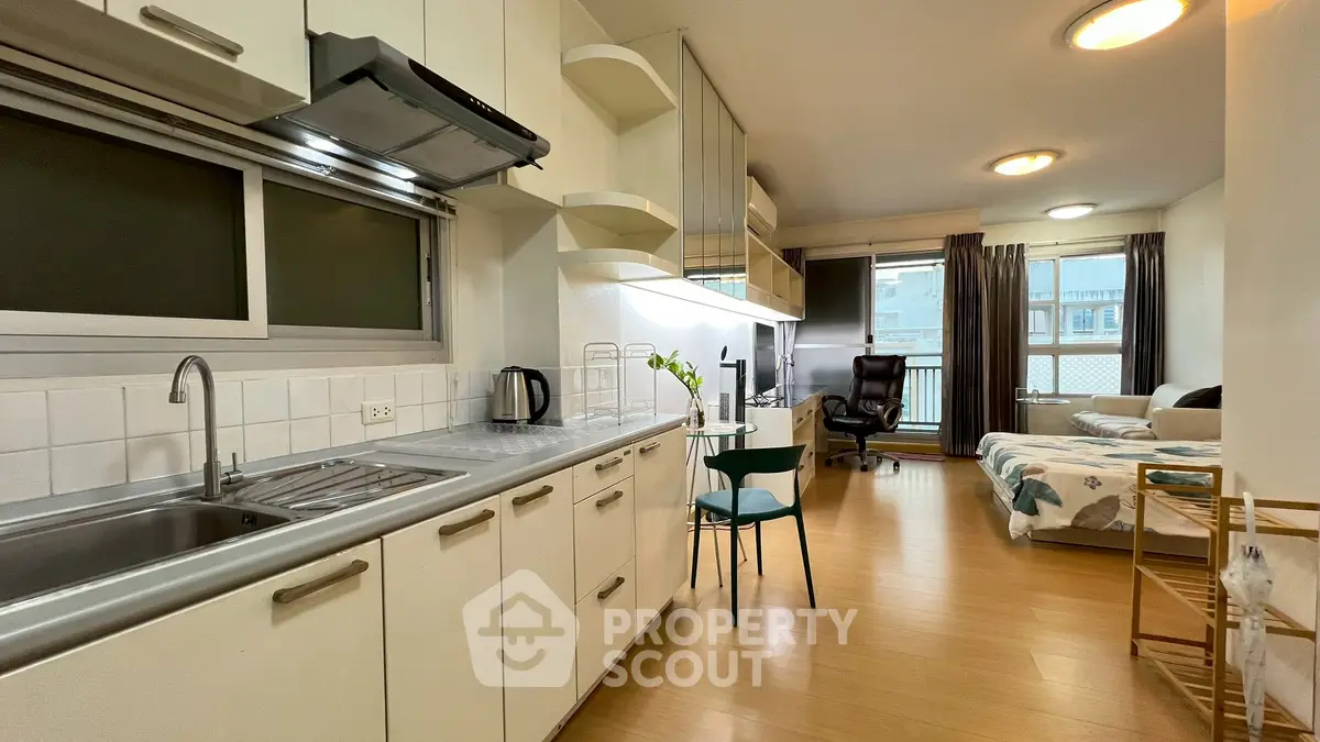 Modern studio apartment with open kitchen and cozy living area, featuring sleek cabinetry and ample natural light.