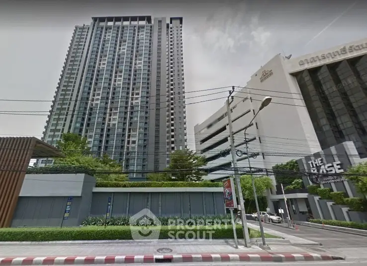 Modern high-rise condominium building with lush greenery and urban surroundings.