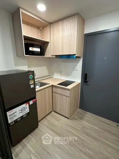 Modern compact kitchen with sleek wooden cabinets and stainless steel appliances in a cozy apartment.