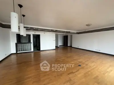 Spacious empty living room with wooden flooring and modern lighting fixtures.
