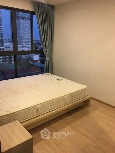 Spacious bedroom with large window offering city view and natural light.