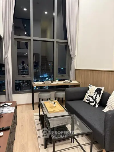 Modern living room with high ceilings and city view, featuring stylish furniture and large windows.