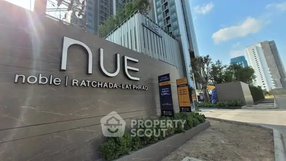 Modern building entrance with NUE Noble Ratchada-Lat Phrao signage and lush greenery.