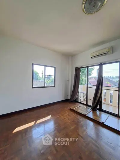 Spacious empty room with wooden flooring and large windows offering natural light and views.