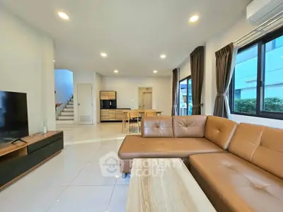 Spacious modern living room with leather sofa and dining area, featuring large windows and elegant decor.