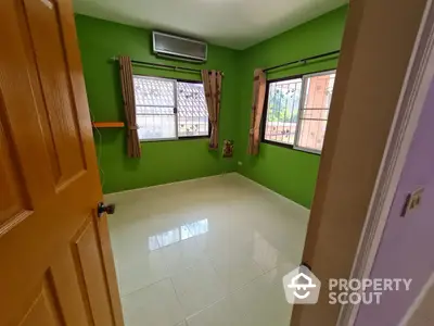 Bright and airy bedroom with vibrant green walls, large windows with burgundy curtains, and glossy white floor tiles, offering a refreshing living space.