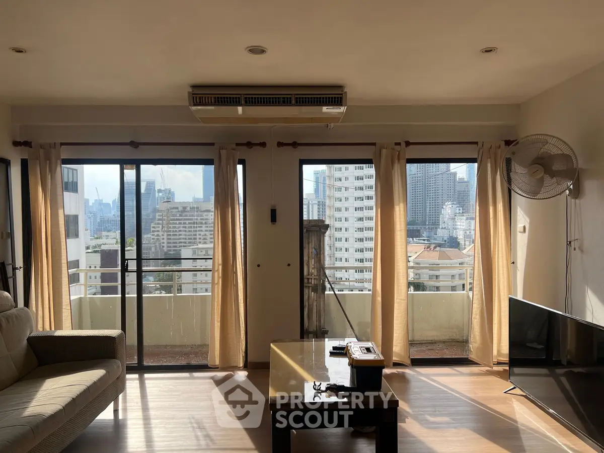 Spacious living room with large windows and city view, featuring modern furniture and natural light.