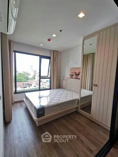 Modern bedroom with large window and city view, featuring a sleek wardrobe and hardwood flooring.