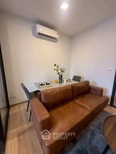 Cozy living room with leather sofa and dining table, featuring modern air conditioning.