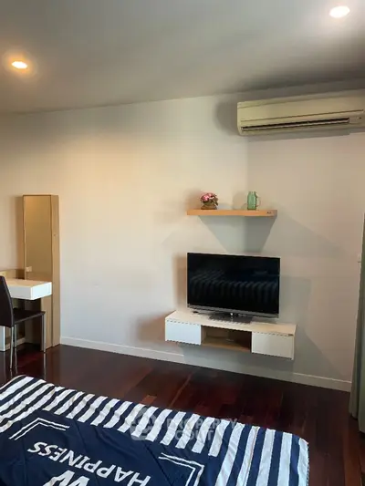 Modern bedroom with TV and air conditioning, featuring sleek wooden flooring and stylish decor.