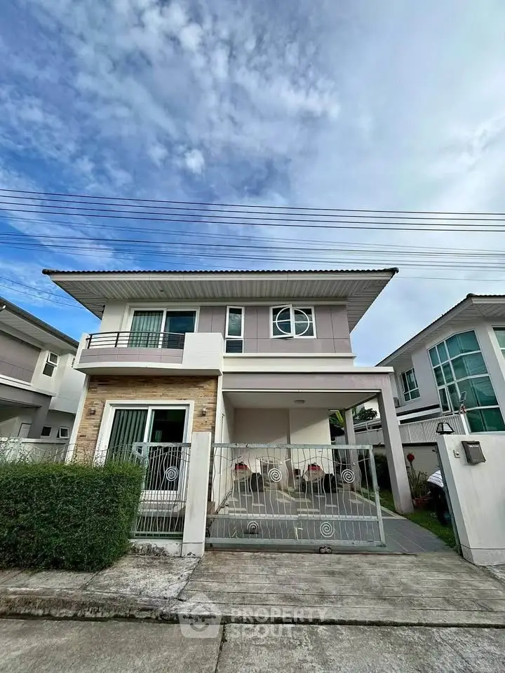 Modern two-story house with gated driveway and contemporary design under a clear blue sky.
