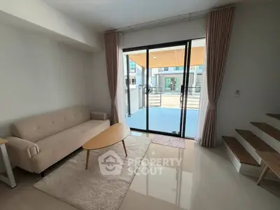 Modern living room with sleek design and large glass doors opening to a patio, featuring a cozy sofa and stylish coffee table.