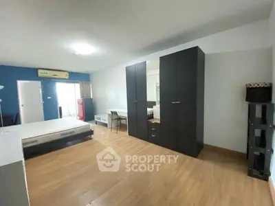 Spacious bedroom with modern furnishings and ample natural light, featuring a large wardrobe and sleek wooden flooring.