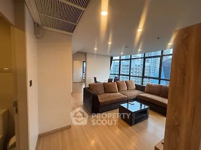 Spacious modern living room with large windows and city view, featuring a cozy sectional sofa and sleek wooden flooring.