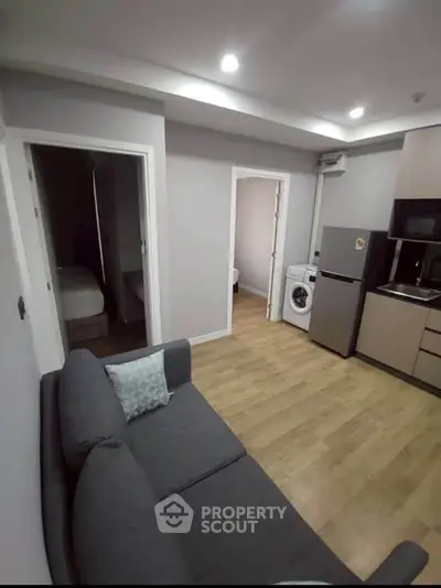 Modern apartment interior with cozy living room and kitchen featuring washing machine and fridge.