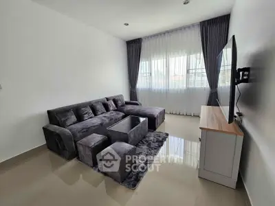Modern living room with sleek gray sofa and wall-mounted TV, featuring large windows and elegant curtains.