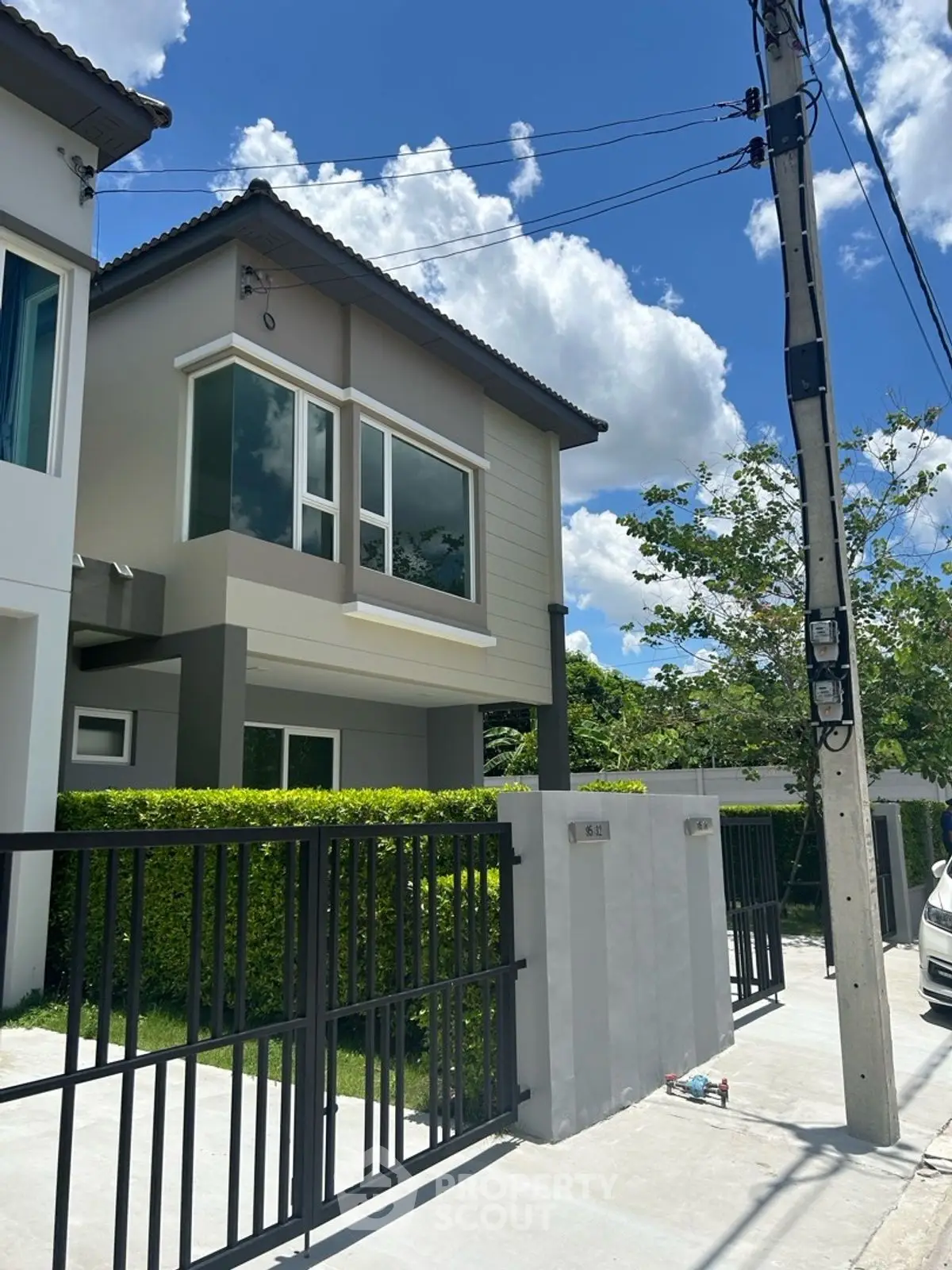 Modern two-story house with sleek design and lush greenery under a bright blue sky.