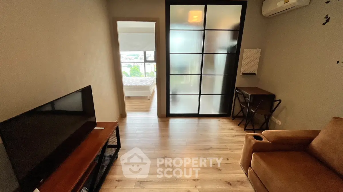 Cozy living room with wooden flooring and modern furniture, leading to a bright bedroom.