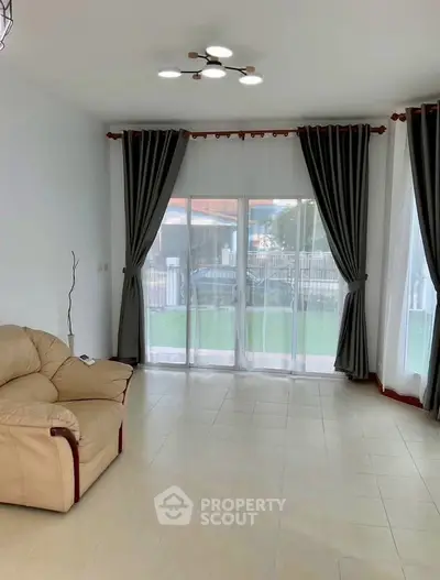Spacious living room with large windows and elegant curtains, featuring a cozy beige sofa and modern lighting.