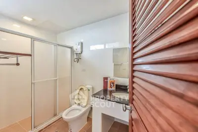 Modern bathroom with shower enclosure and wooden door, featuring sleek fixtures and ample lighting.