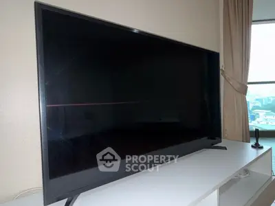Modern living room with large flat-screen TV and city view window.