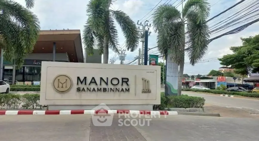 Entrance sign of Manor Sanambinnam with palm trees and street view.