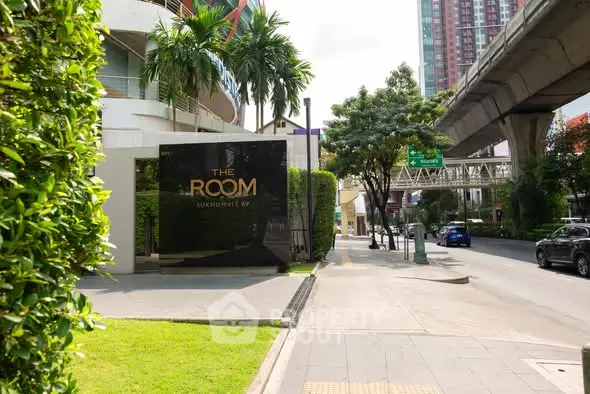 Modern urban street view with luxury condominium entrance and lush greenery.