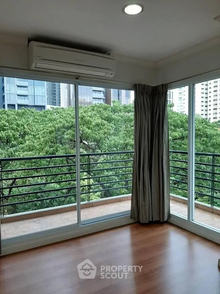 Spacious corner unit with large windows and balcony offering lush green views in urban setting.