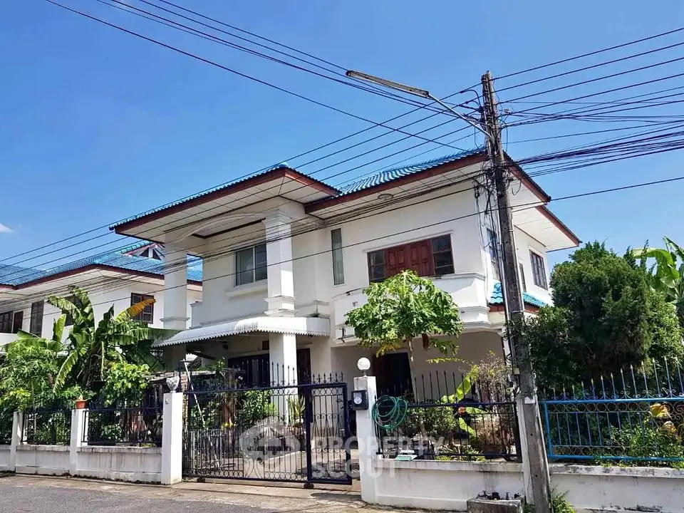 Charming two-story house with lush garden and secure gated entrance in a serene neighborhood.