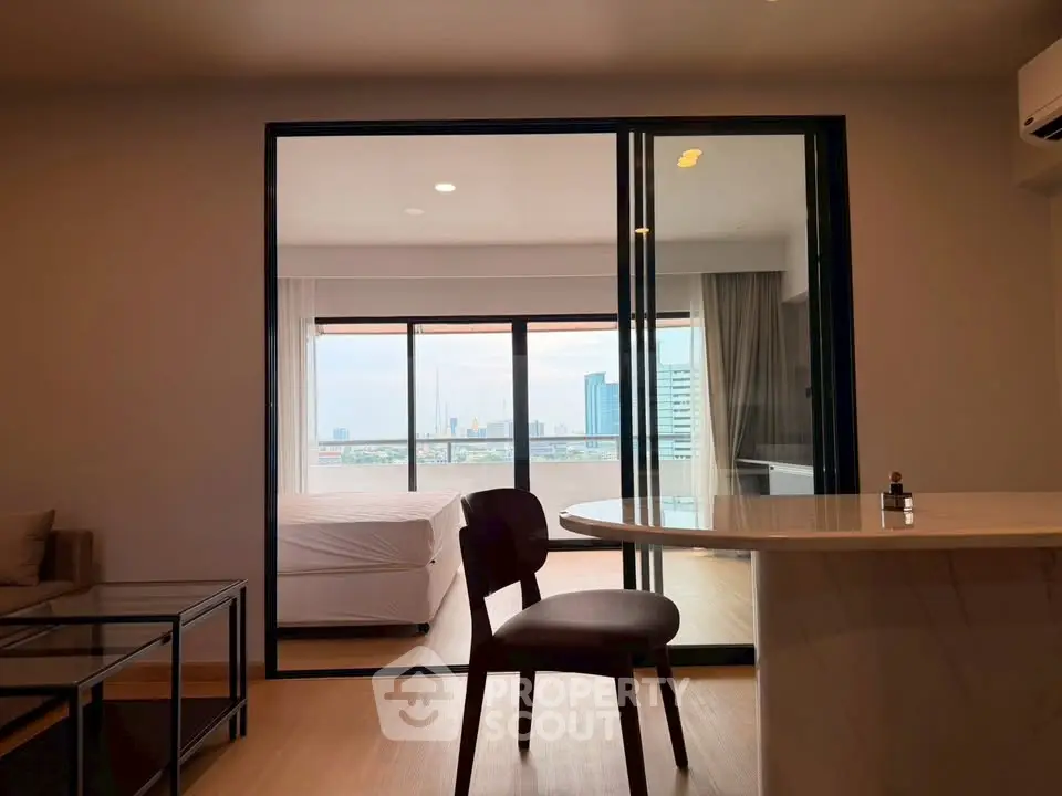 Modern open-plan living room with city view and sliding glass doors leading to a bedroom.