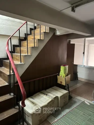 Spacious interior with a modern wooden staircase and a unique red handrail, complemented by natural light from the adjacent window.