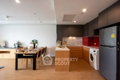 Modern open-plan kitchen with dining area and washing machine, featuring sleek cabinetry and wood flooring.