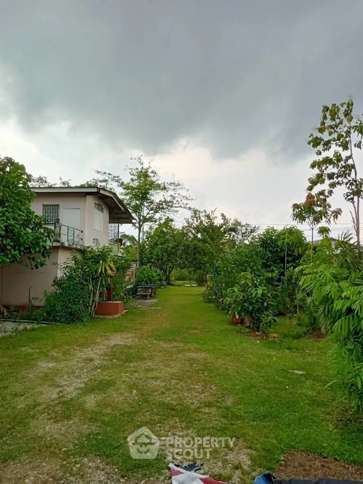 Charming countryside property with lush garden and cozy house under cloudy sky.