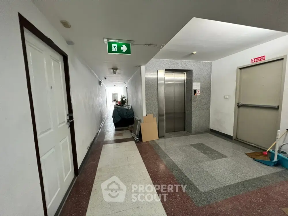 Spacious apartment corridor with elevator access and emergency exit signs.