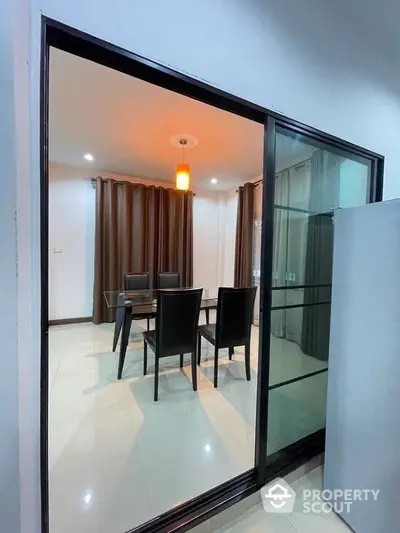 Modern dining room with glass table and elegant chairs, featuring ambient lighting and floor-to-ceiling curtains.