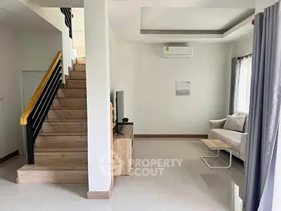 Modern living room with staircase and sleek furniture in a bright, airy space.