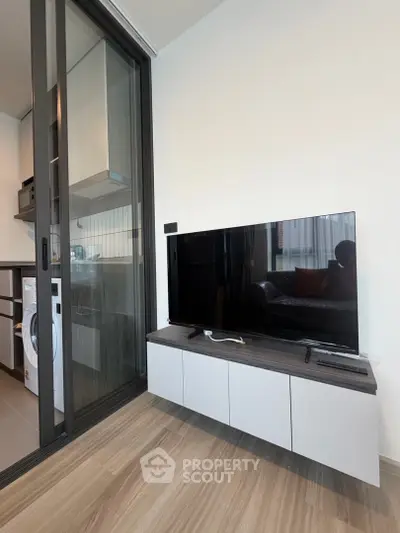 Modern living room with sleek TV setup and sliding glass door to kitchen area.