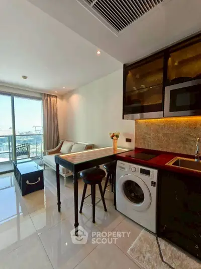 Modern open-plan kitchen and living area with balcony view, featuring washing machine and stylish decor.
