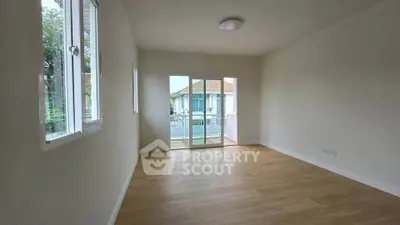 Spacious empty room with wooden flooring and large windows offering natural light and balcony access.
