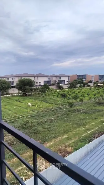 Scenic view from balcony overlooking lush green fields and modern residential houses.