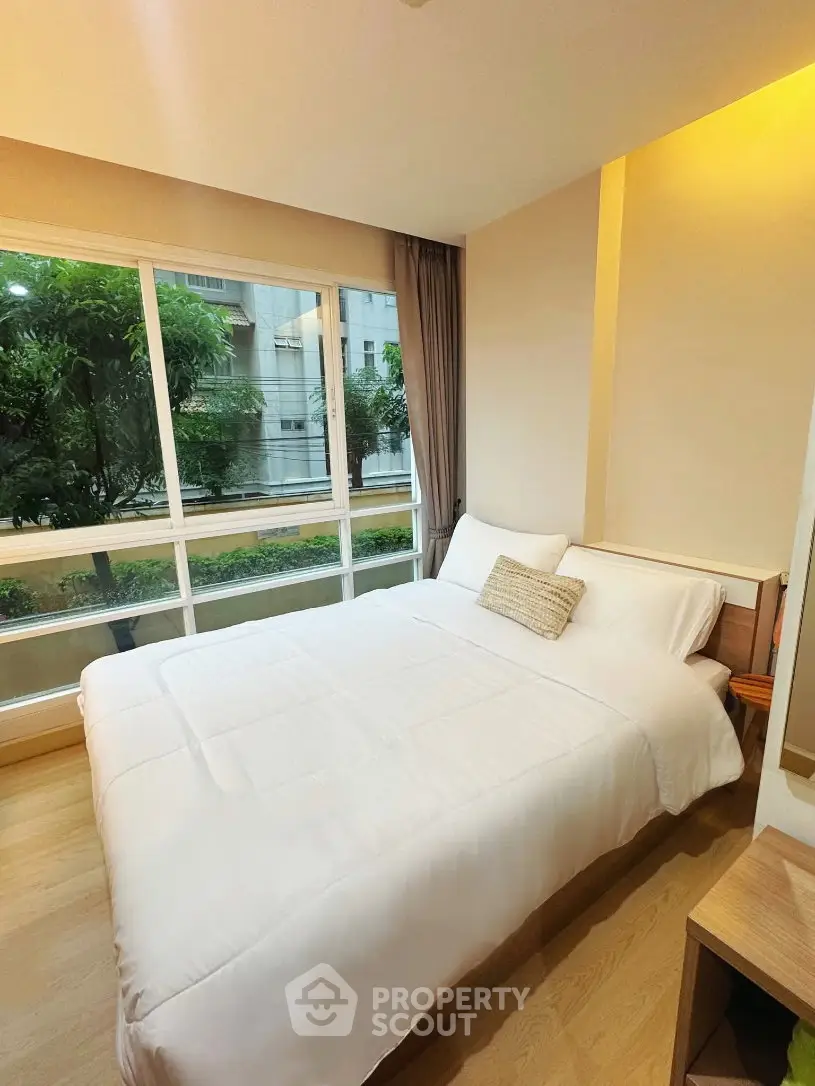 Cozy bedroom with large window offering a serene garden view, perfect for relaxation and comfort.