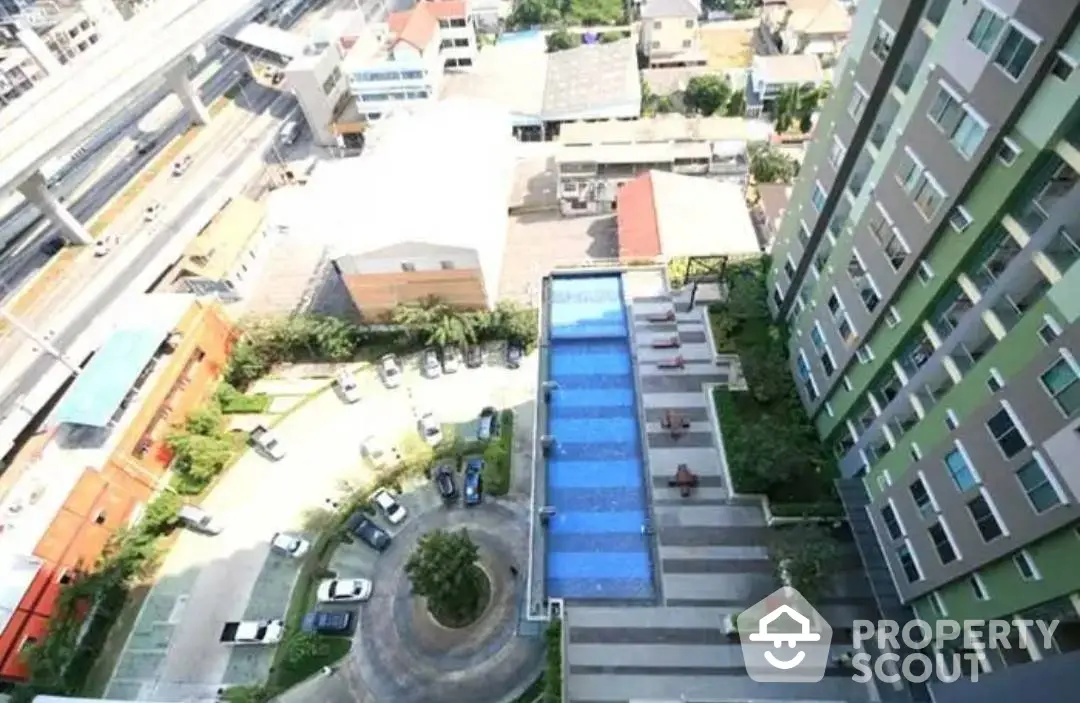 Aerial view of a modern residential building with a large outdoor swimming pool, landscaped garden, and convenient city access.