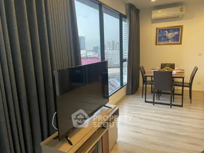 Modern living room with large windows and city view, featuring a sleek TV and dining area.
