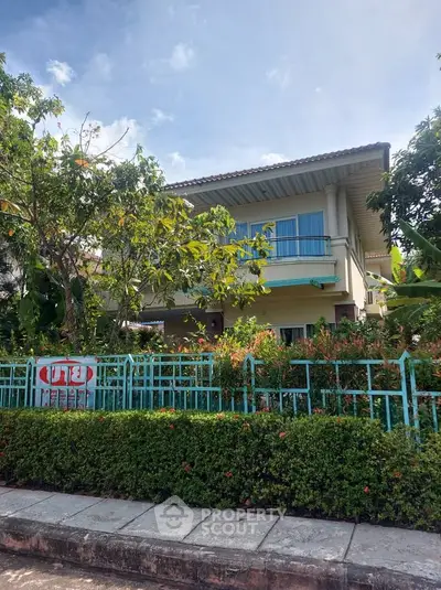 Charming two-story house with lush garden and blue fence, perfect for family living.