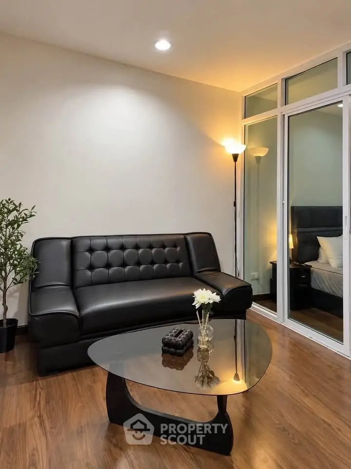 Modern living room with sleek black sofa and glass coffee table, adjacent to a cozy bedroom.