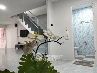 Modern open-plan living area with staircase and bathroom, featuring sleek design and floral decor.
