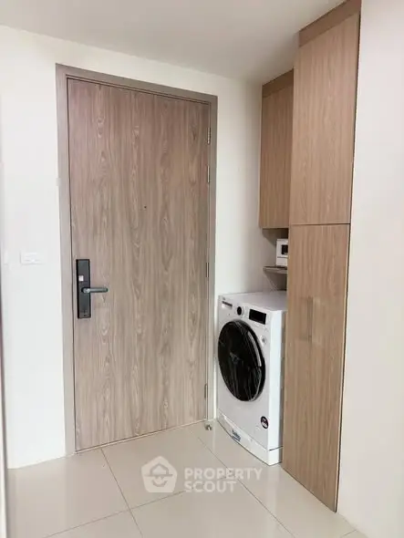 Modern laundry area with washing machine and wooden cabinetry in sleek apartment.